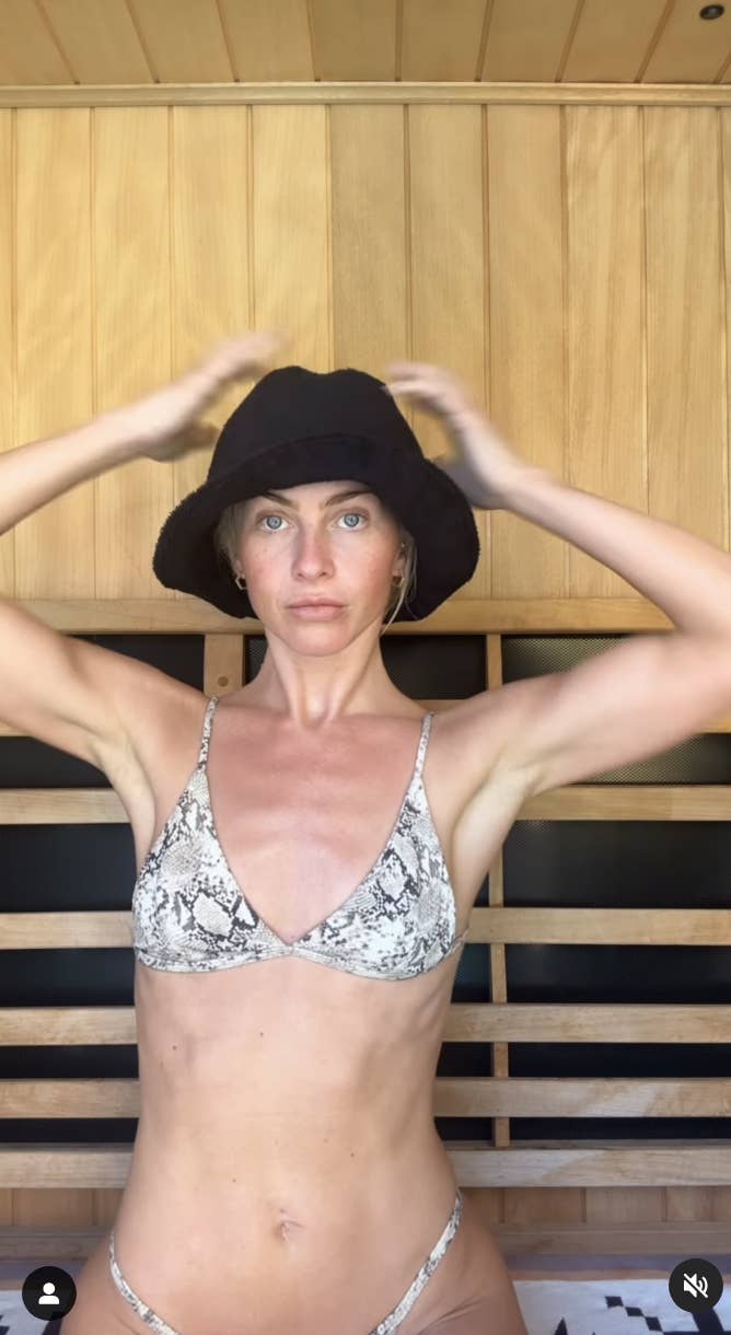 A woman in a bikini and a bucket hat touches her hat in a wooden room