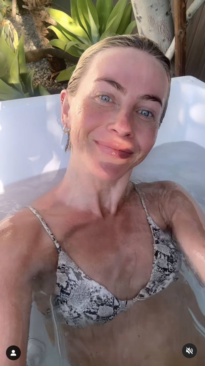 A woman in a snake print bikini smiling in a hot tub with greenery in the background.