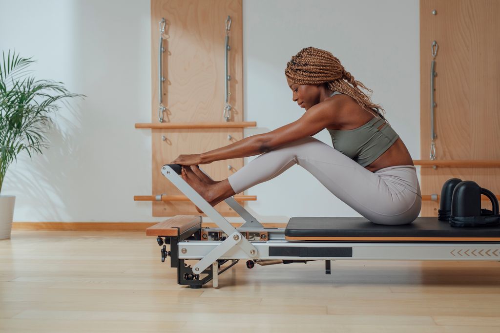     a woman touching her toes while doing a pilates exercise on the reformer.