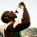 A man in athletic apparel squeezes water into his mouth from a water bottle