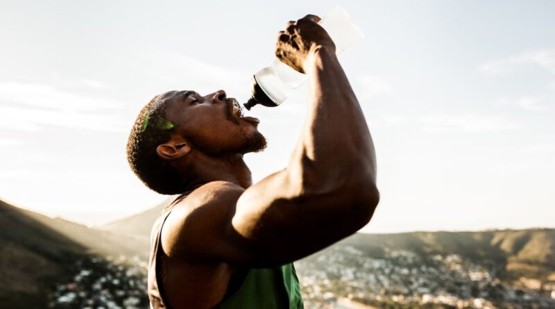 A man in athletic apparel squeezes water into his mouth from a water bottle